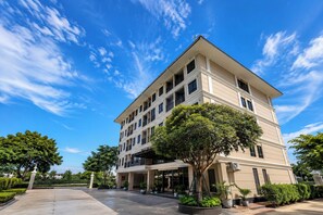 A multi-story hotel with a covered entrance, large windows, and a well-maintained garden. - Baan Thanakul Suvarnabhumi (Bang Phli)