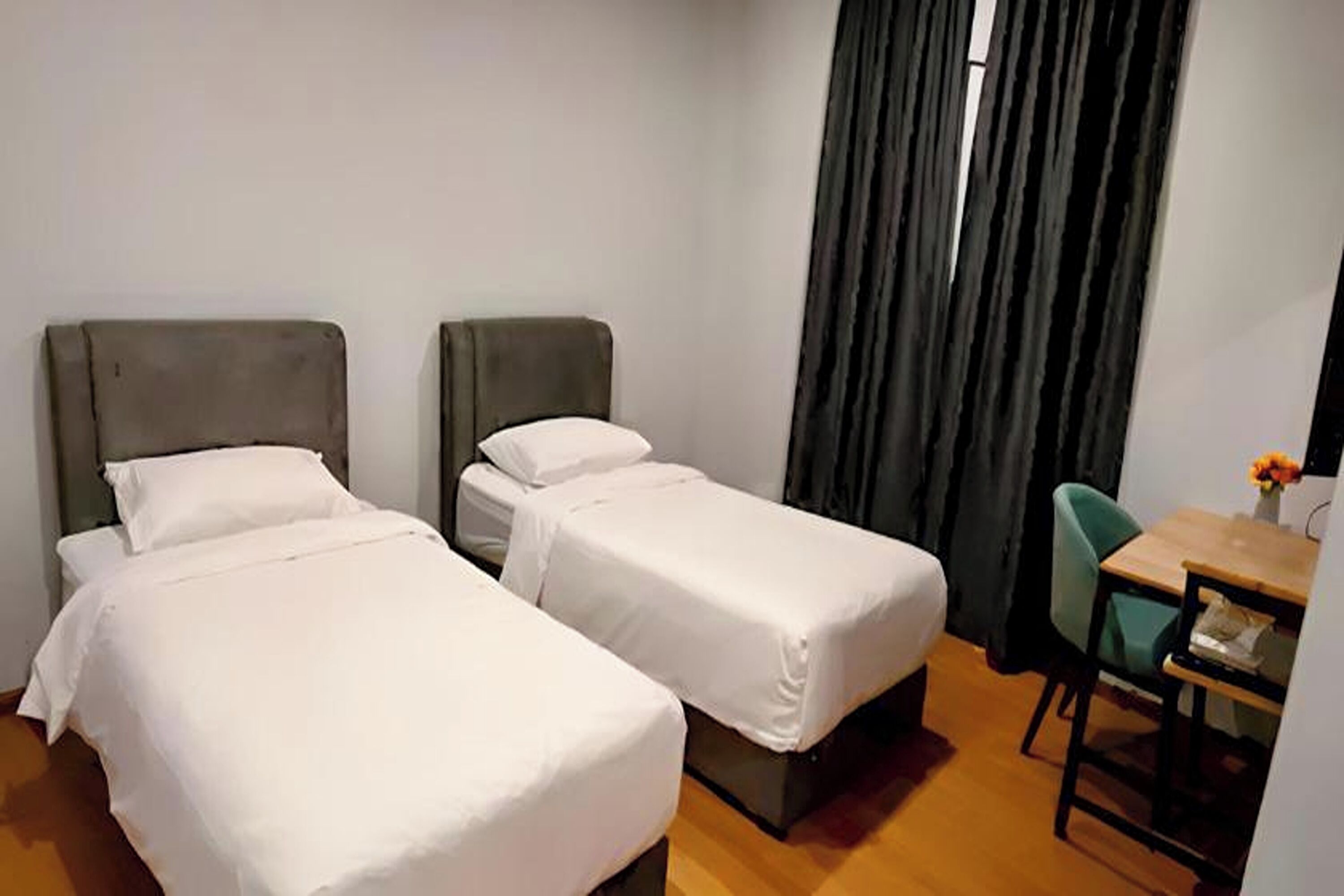 A hotel room with two single beds, a small desk with a chair, and a window with curtains.