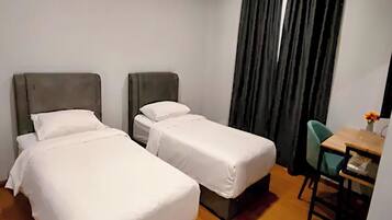 A hotel room with two single beds, a small desk with a chair, and a window with curtains.