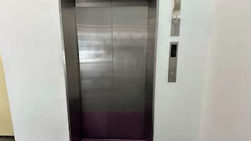 A metallic elevator with a purple carpet, a wall-mounted intercom, and a small ventilation panel.
