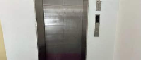 A metallic elevator with a purple carpet, a wall-mounted intercom, and a small ventilation panel.