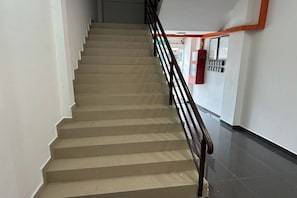 Een trap met een leuning, een brandblusser en een prikbord met aankondigingen aan de muur.