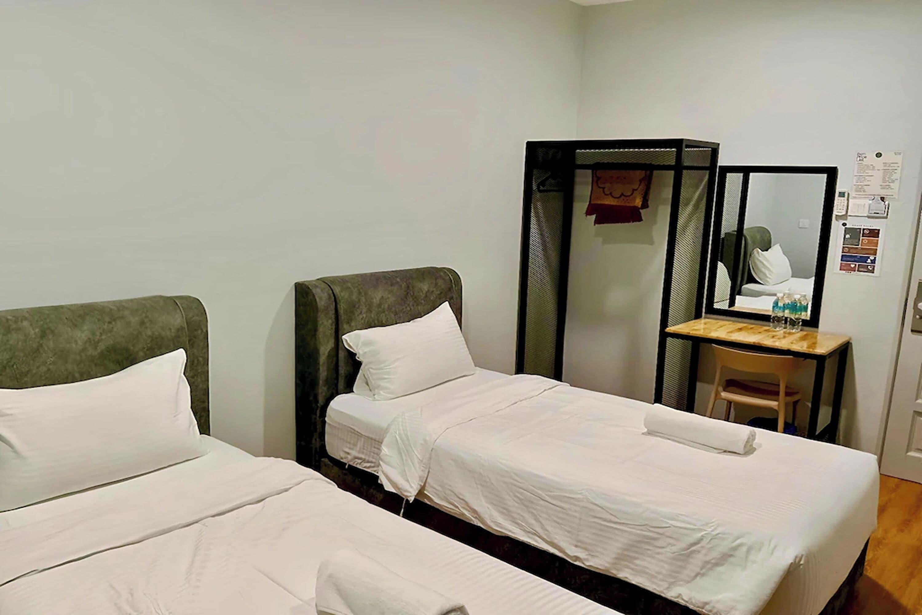 A hotel room with two single beds, a desk with a chair, a mirror, and a small table with items on it.