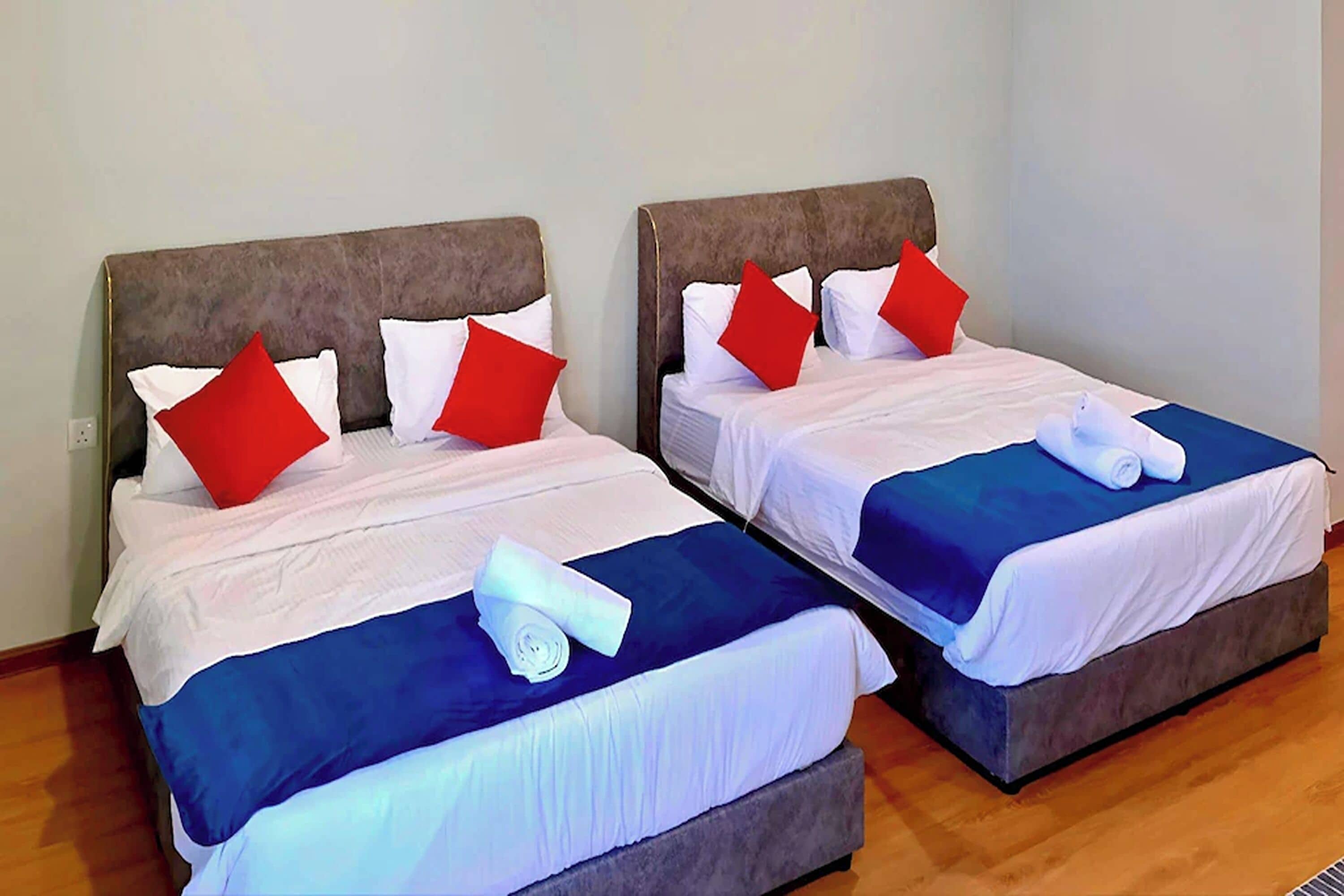 Dos camas individuales con cabeceras, ropa de cama blanca, almohadas rojas y colchas azules.