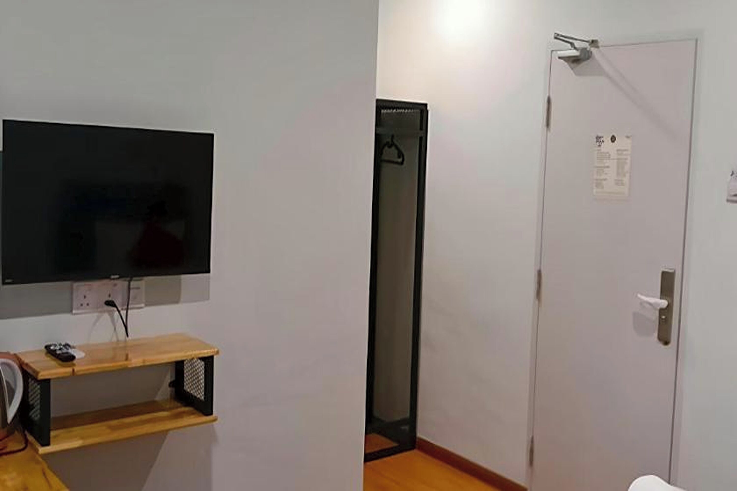 Una habitación con televisión sobre un soporte de madera, una puerta con un aviso y un armario.