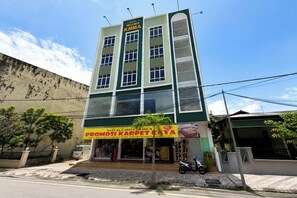 Un edificio de varios pisos con fachada verde y blanca, un letrero que dice 'WISMA KMMA' y una tienda que ofrece 'PROMOSI KARPET KAYA'.