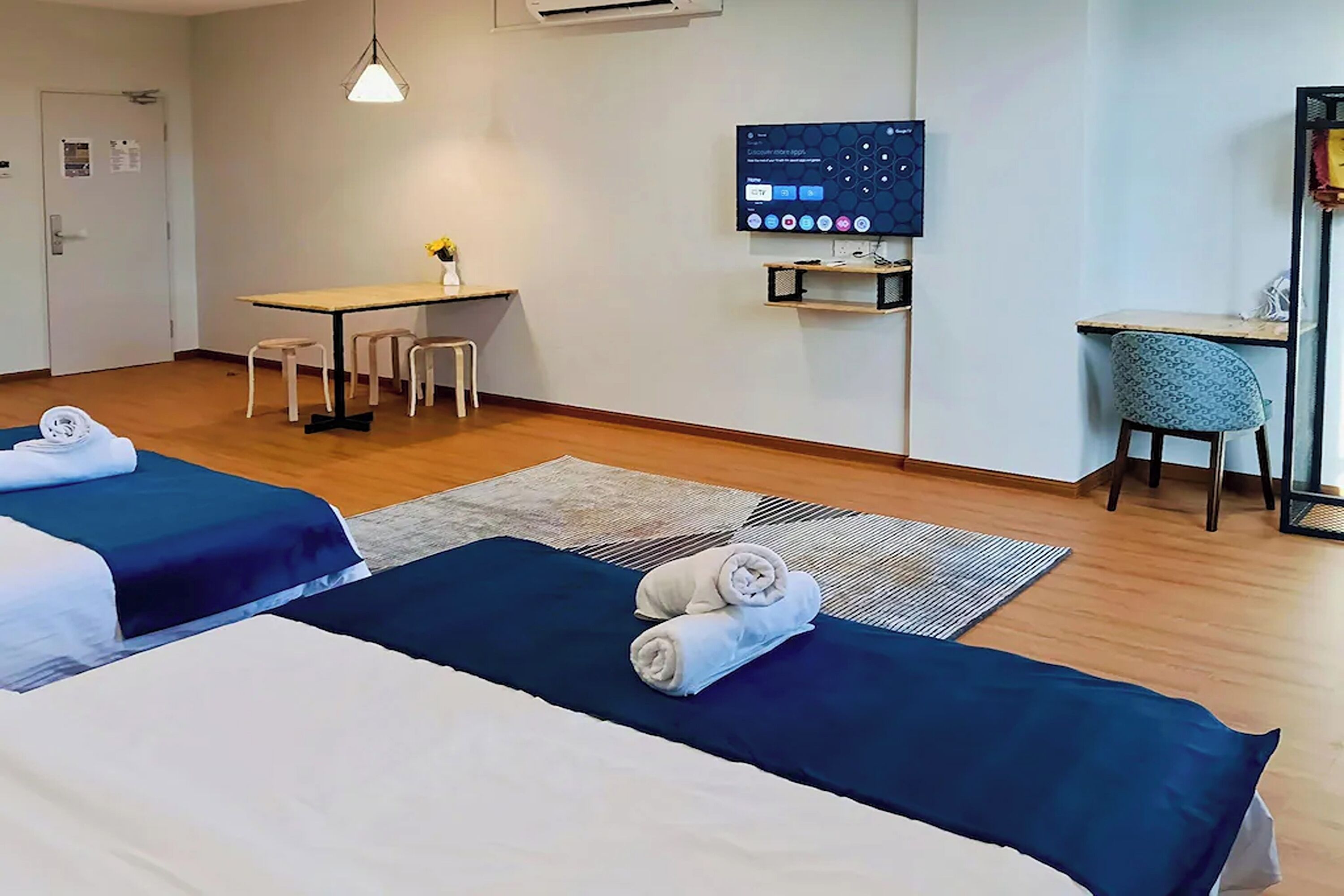 A hotel room with two beds, a desk, a chair, a TV, and a small table with a vase.