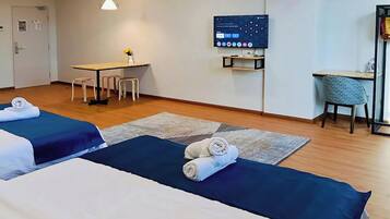 A hotel room with two beds, a desk, a chair, a TV, and a small table with a vase.