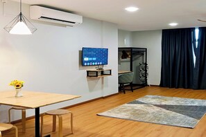 Una sala de estar moderna con piso de madera, una mesa de comedor con sillas, un televisor montado en la pared y un ventanal con cortinas.