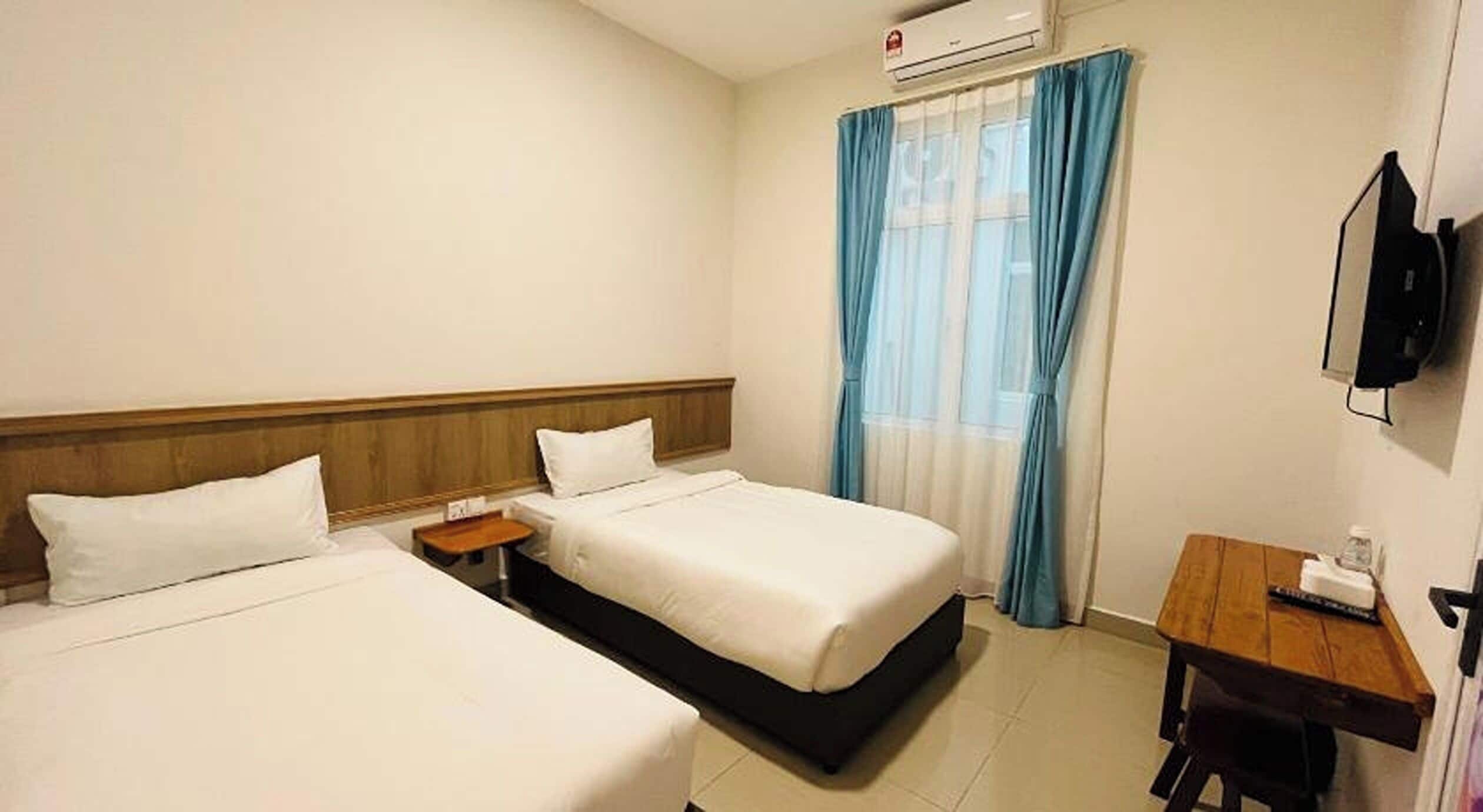 A hotel room with two beds, a desk, a chair, a TV, and an air conditioning unit.