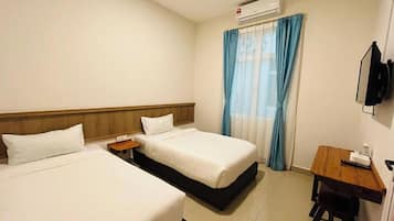 A hotel room with two beds, a desk, a chair, a TV, and an air conditioning unit.