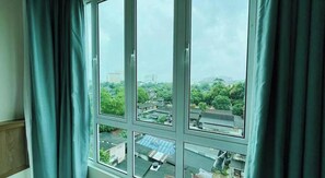 A room with a large window, curtains, and a view of a residential area. - Alexis Kt Roomstay (Kuala Terengganu)