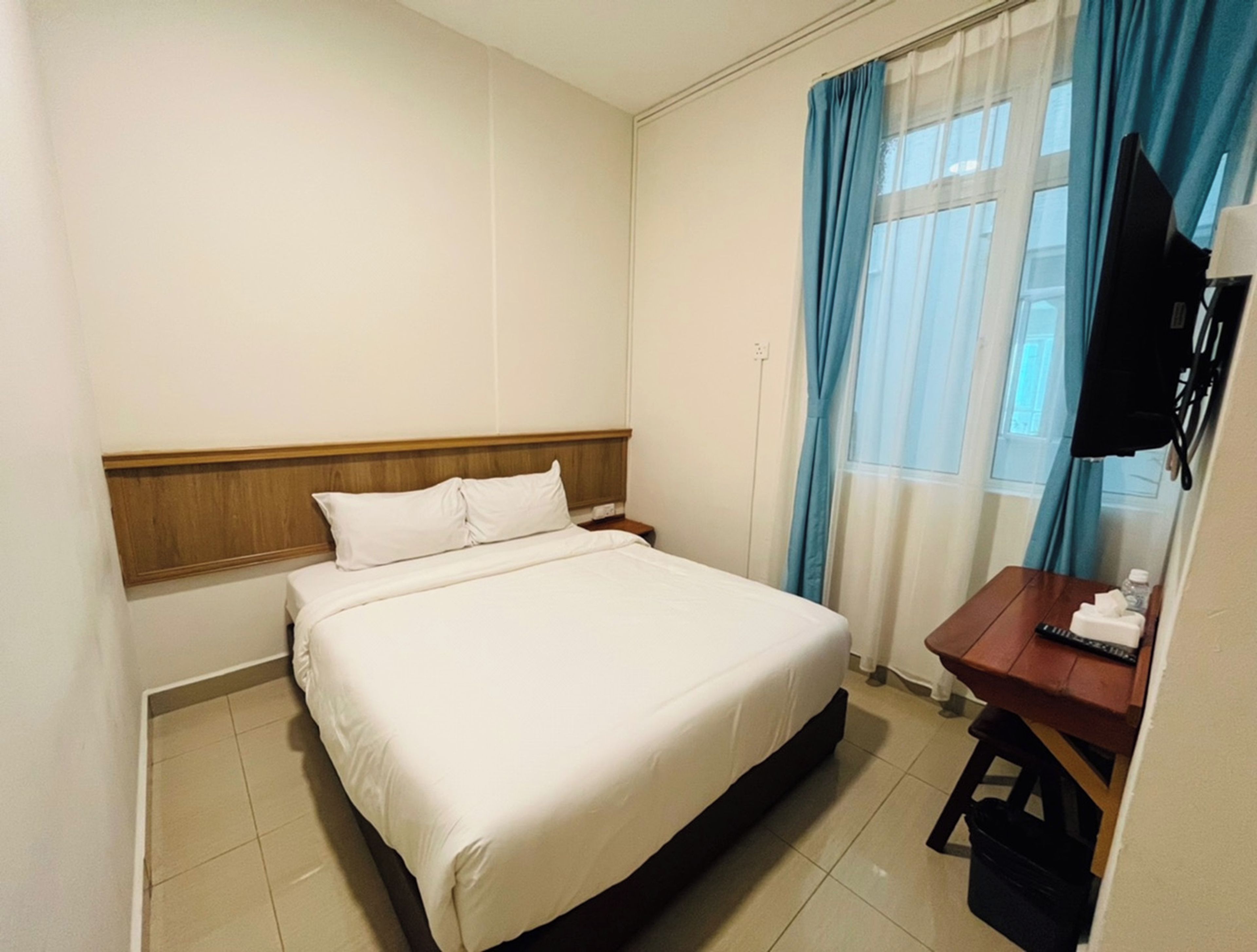 A hotel room with a bed, a desk, a television, and a window with curtains.