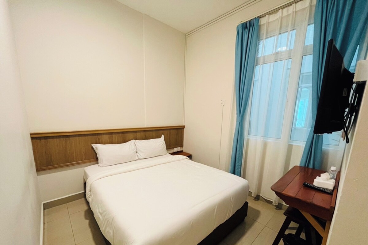 Habitación de hotel con cama, escritorio, televisor y ventana con cortinas.