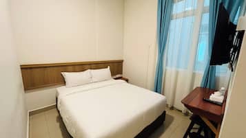 A hotel room with a bed, a desk, a television, and a window with curtains.