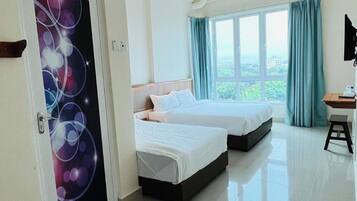 A hotel room with two beds, a desk, and a view of greenery outside.