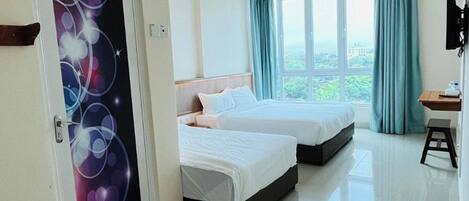 A hotel room with two beds, a desk, and a view of greenery outside.