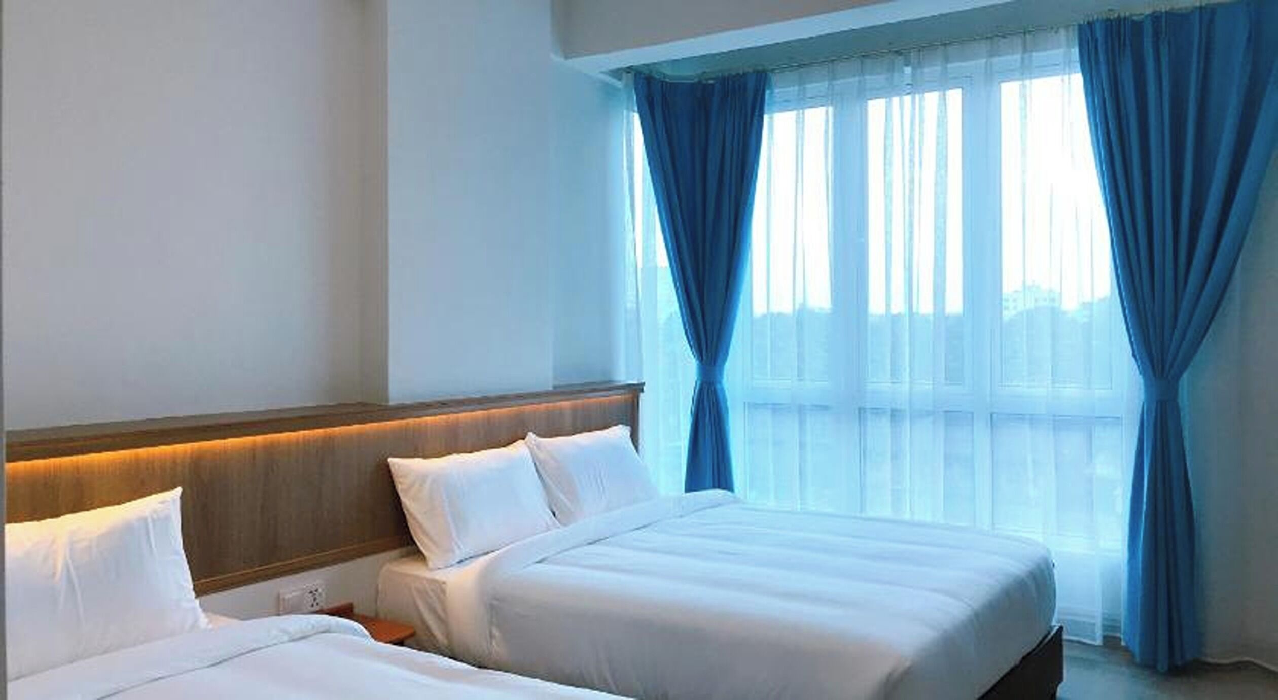 A hotel room with two beds, a wooden headboard, and large windows with blue curtains.