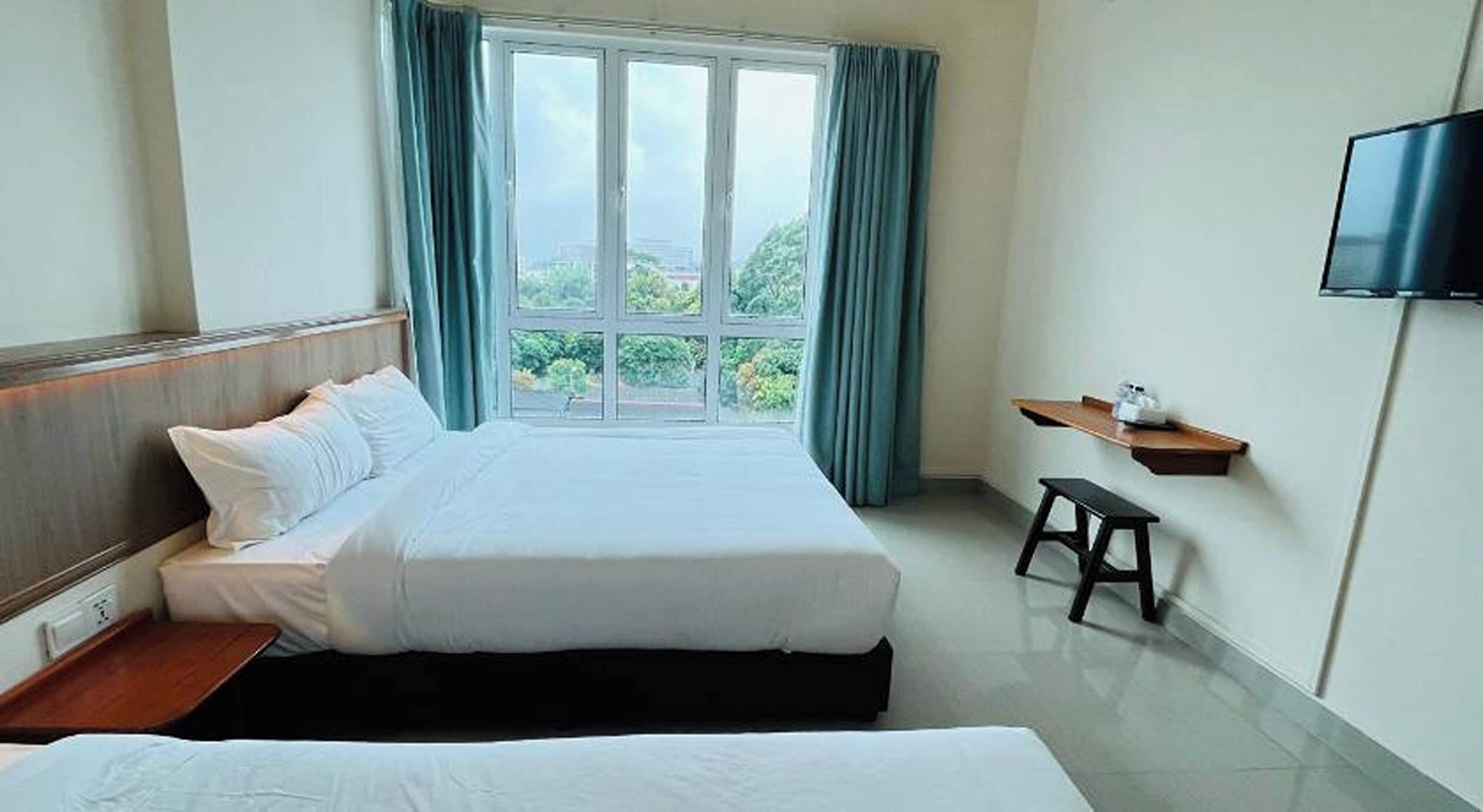 A hotel room with a large bed, a TV mounted on the wall, and a window with curtains.