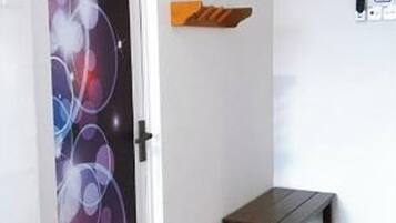 A room with a door featuring a colorful abstract design, a small wooden bench, and a wall-mounted shelf.