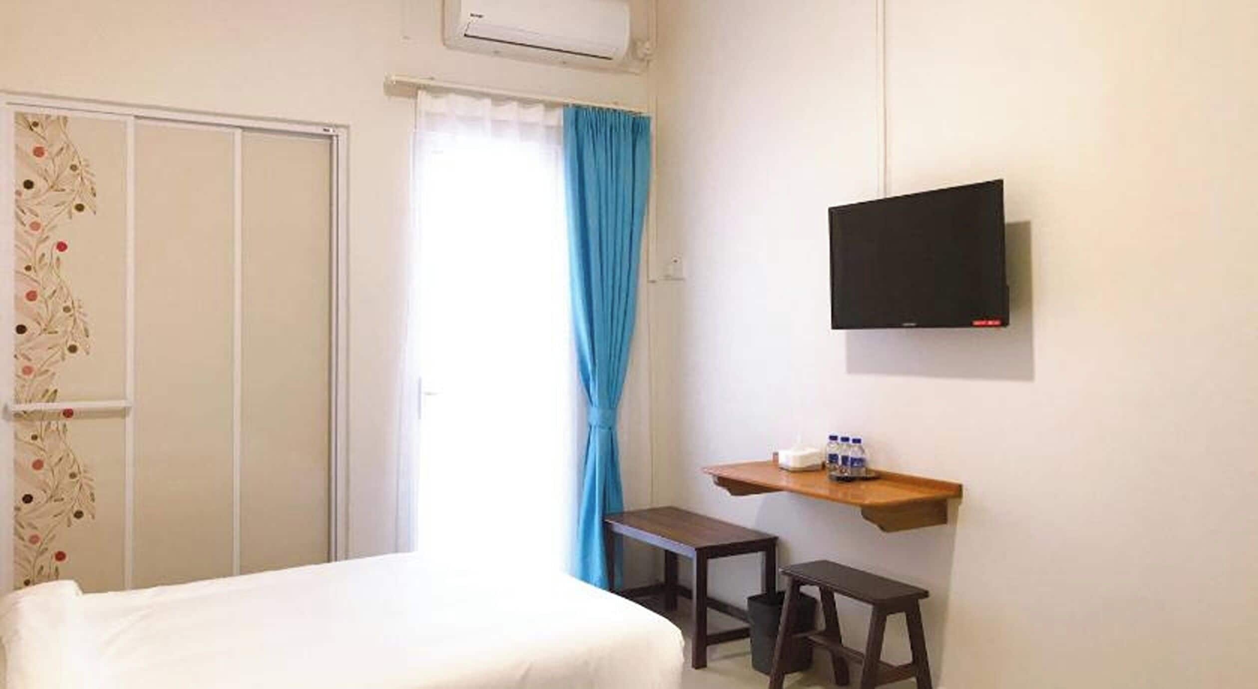 A hotel room with a bed, a desk, two stools, a TV, and a window with curtains.