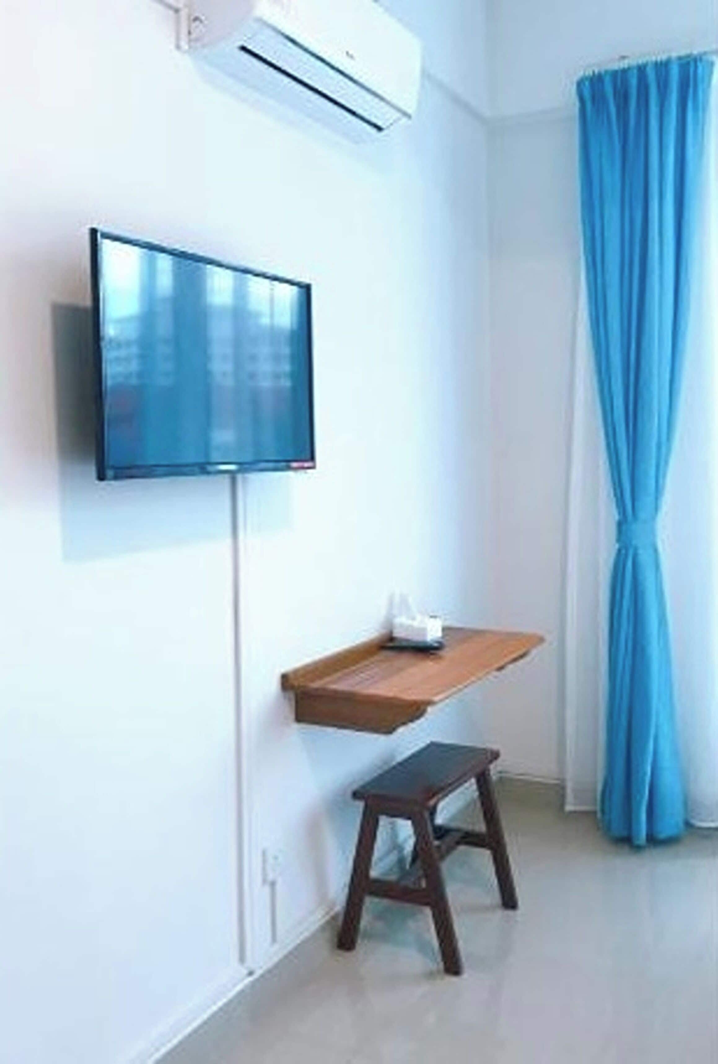 A room with a mounted television, a small wooden table, a step stool, and a blue curtain.