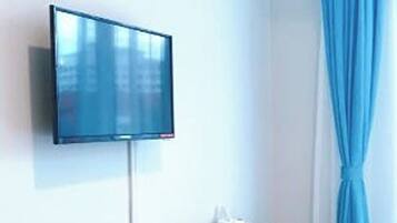 A room with a mounted television, a small wooden table, a step stool, and a blue curtain.