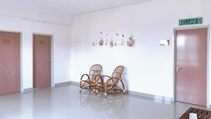 A hallway with two doors, one labeled '403' and another with a green sign reading 'KELUAR'. There are wicker chairs in the center and a small table at the end of the hallway.