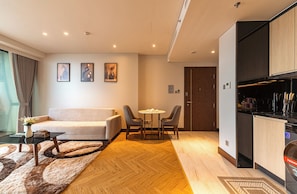 Uma sala de estar moderna com um sofá, duas cadeiras, uma mesa de centro e uma mesa de jantar. Há uma área de cozinha com uma geladeira e um micro-ondas.