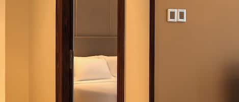 Une chambre d’hôtel avec un plancher en bois, un lit avec une literie blanche, un miroir, un vase de fleurs et une petite table.