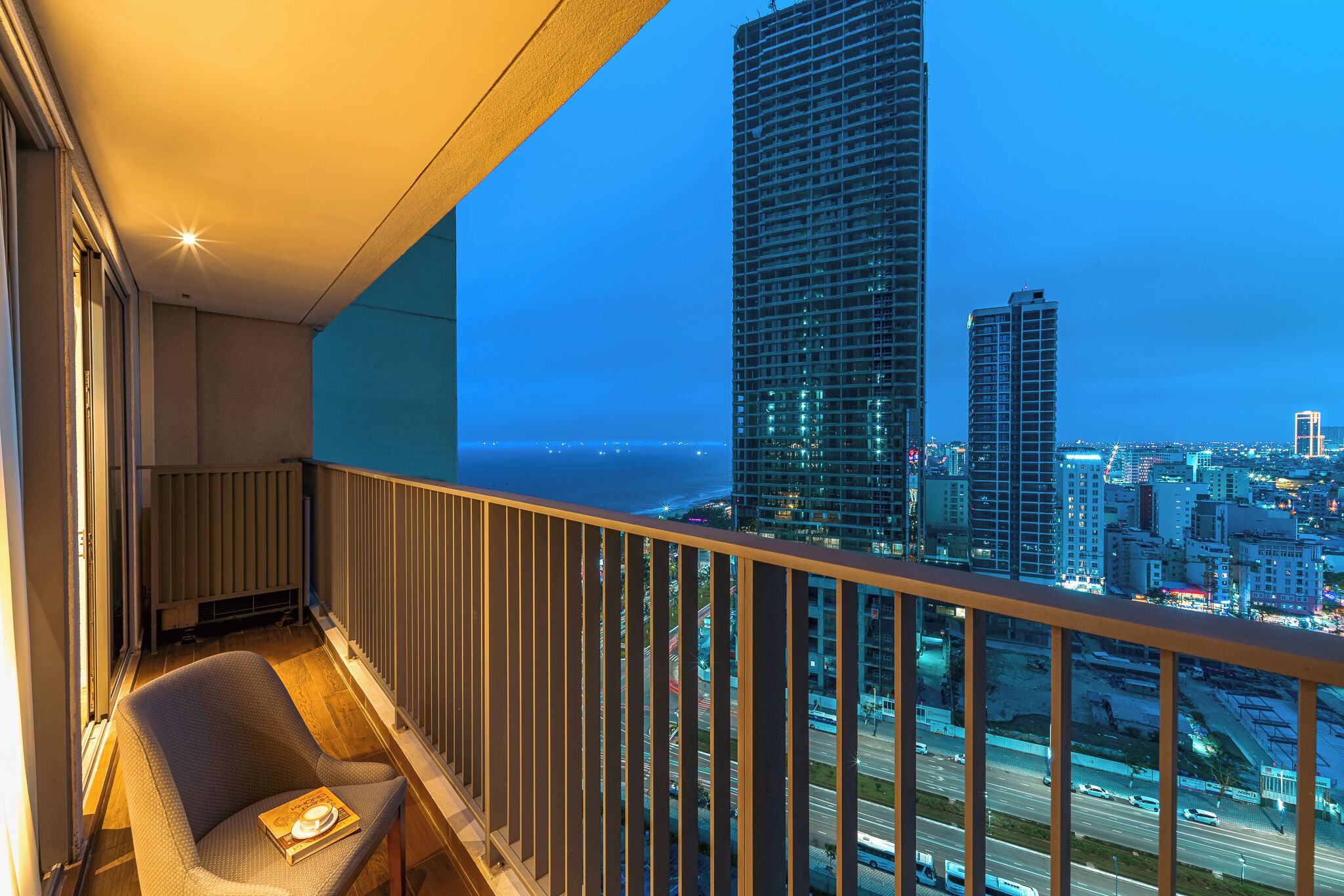 A balcony with a view of a cityscape and the ocean at dusk.