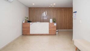 Un mostrador de recepción con detalles de madera, una pared blanca con un panel vertical de madera y un suelo de baldosas.