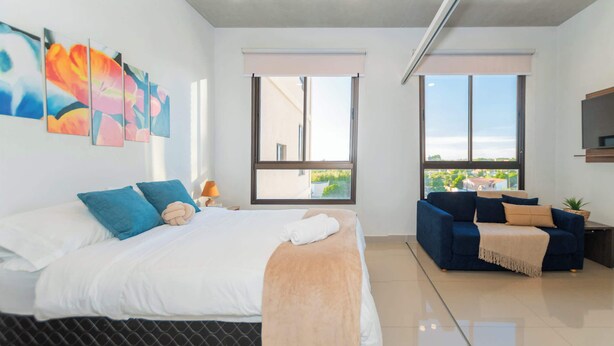 Un dormitorio moderno con una cama grande, un sofá y dos ventanas que ofrecen vistas al exterior.