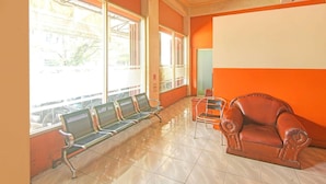 Une salle d’attente avec des chaises en métal et un fauteuil en cuir, de grandes fenêtres et un sol carrelé.