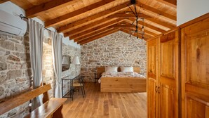 A rustic bedroom with stone walls, wooden beams, a bed, a desk, and a bench. - Old House Grota by Villas Guide (Umag)