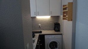 Een kleine keuken met witte kasten, een koffiezetapparaat en een wasmachine.