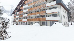 Monikerroksinen hotelli, jossa on parvekkeet, lumipeitteiset ympäristöt ja vuoristomaisema taustalla.