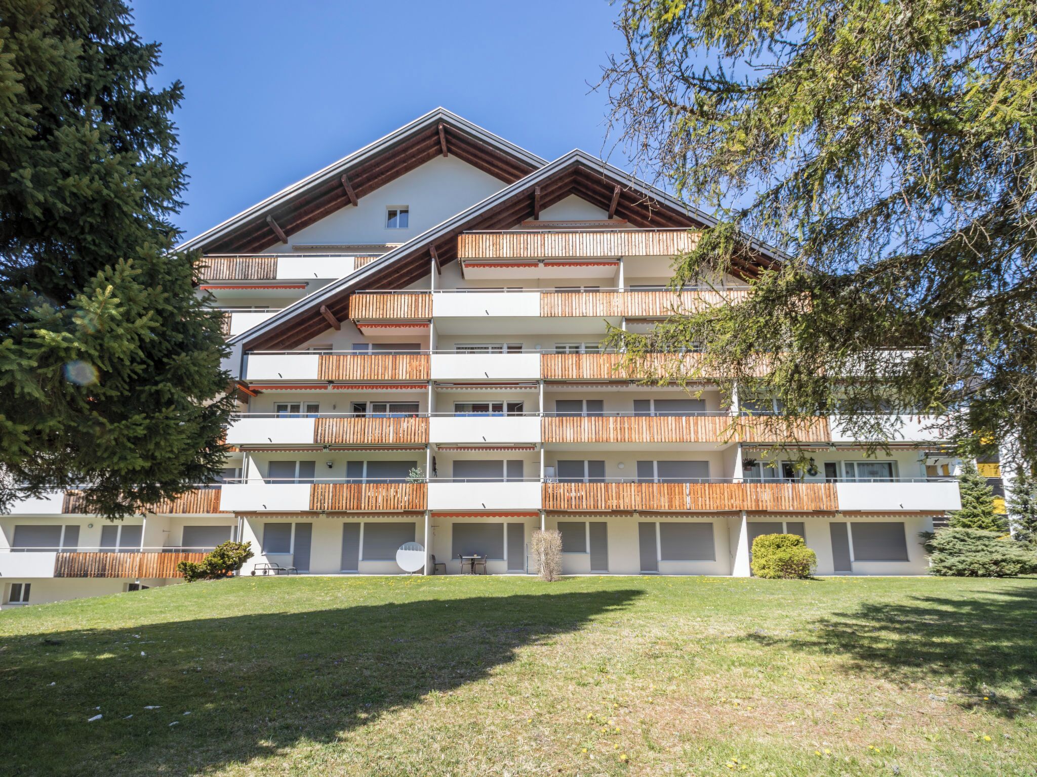 A multi-story hotel with balconies, a flat roof, and a grassy front yard.