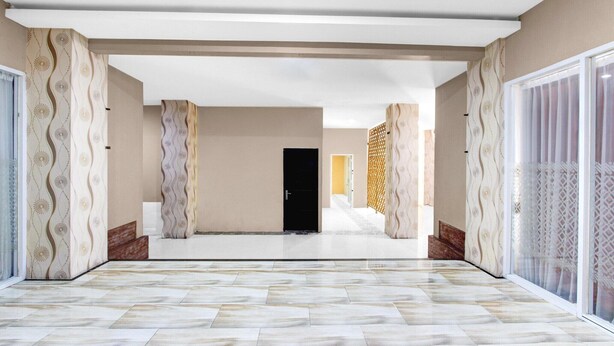 A spacious hallway with patterned walls, a marble floor, and a black door at the end.
