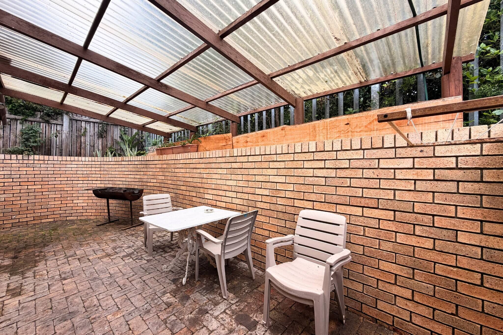 A covered patio with a brick wall, a grill, and a table with chairs.
