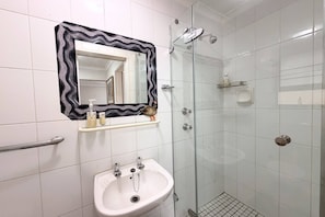 Ein Badezimmer mit weißem Waschbecken, einem Spiegel mit schwarzem Rahmen, einer Dusche und einer Haltestange.