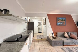 Eine moderne Küche mit Einbauherd, Spüle und Arbeitsplatte. Ein Flur führt zu einem Badezimmer sowie zu einem Wohnbereich mit Sofa und einem Gemälde.