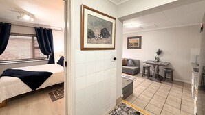 A room with a bed, a small table, a sofa, and a painting on the wall. - Serene 1-bedroom Apartment in Plettenberg Bay - Guinea's Nest (Plettenberg Bay)