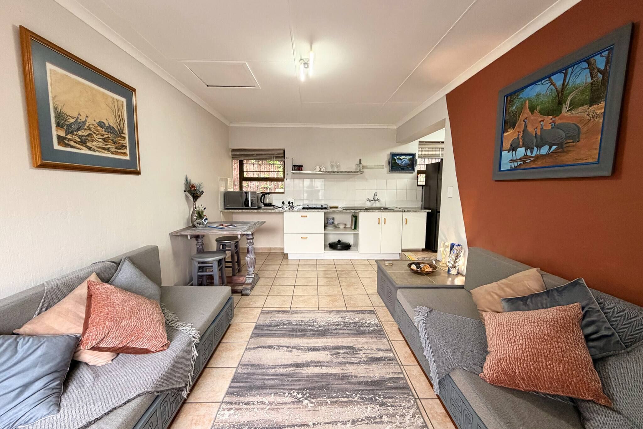 A living room with two sofas, a kitchen in the background, and artwork on the walls.