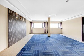 Una habitación amplia con un papel tapiz estampado, una alfombra azul y ventanas grandes.