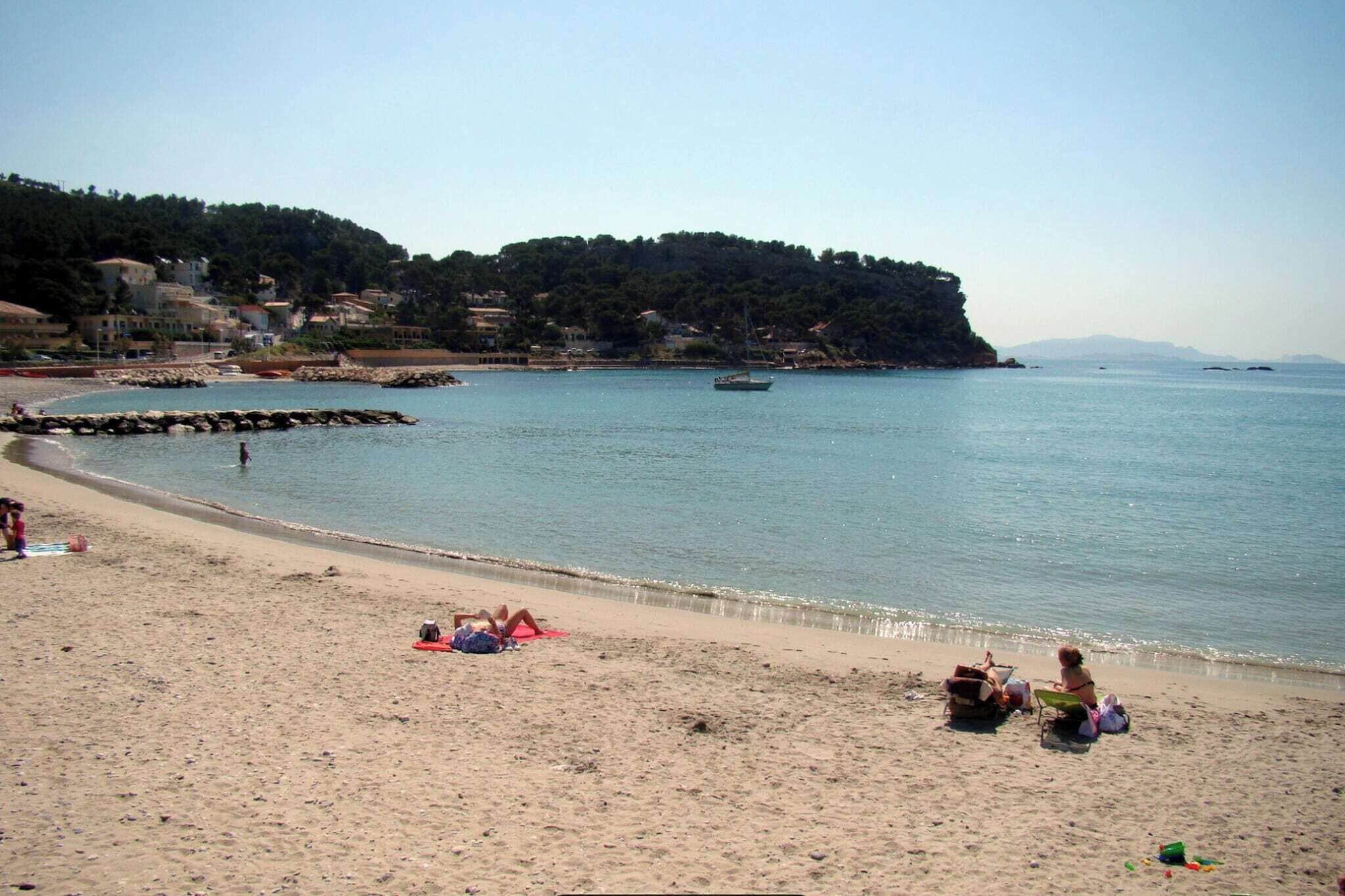 A beach with a rocky breakwater, calm sea, and buildings in the background.