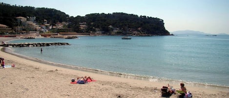 A beach with a rocky breakwater, calm sea, and buildings in the background.