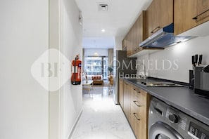 A modern kitchen with wooden cabinets, a built-in oven, and a washing machine. - Bloomfields Studio Oasis Masdar (Abu Dhabi)