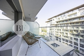 Ein moderner Hotelbalkon mit Korbstühlen und einem kleinen Tisch, mit Blick auf ein Hochhaus.