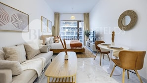 A modern living room with a sofa, coffee table, dining table, and chairs. There is a bed with a view to the outside. - Bloomfields Studio Oasis Masdar (Abu Dhabi)